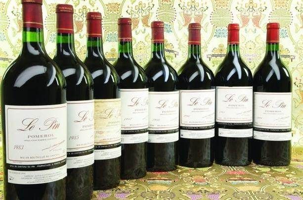 Six bottles of red wine, including exotic Chateu Le Pin, are lined up on a table.