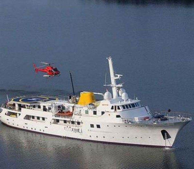 A large white boat with a helicopter flying over it, offering an extravagant family vacation on one of the most luxurious yachts in the world.