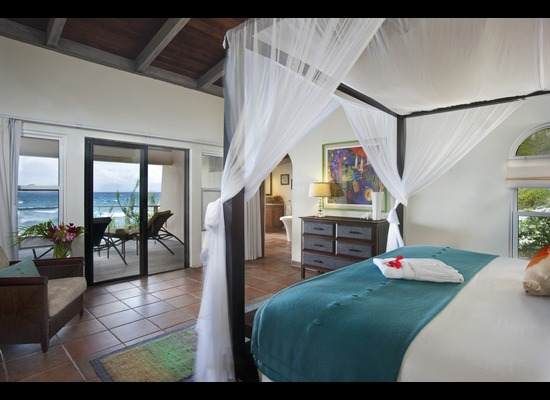 A bedroom with a canopy bed and a view of the ocean at Biras Creek resort.