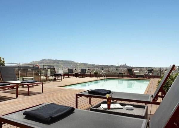 A rooftop pool with lounge chairs and a view of the city, perfect for enjoying a rooftop drink in Barcelona.