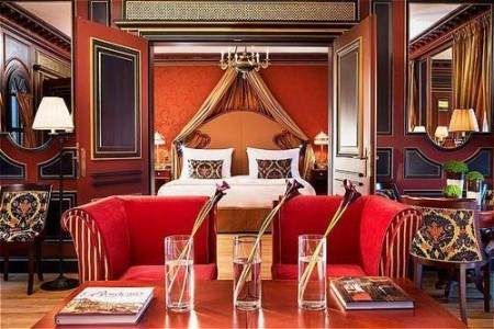 An ornate bedroom with red chairs and a bed featuring historical elegance and the color Bordeaux.