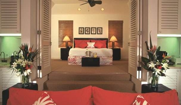 Be a member of the cottage colony at Cambridge Beaches Resort and Spa with a bedroom featuring a large bed and red pillows.