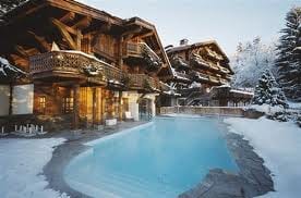 A wooden house with a swimming pool in the snow, offering spa massages with beautiful landscape views.