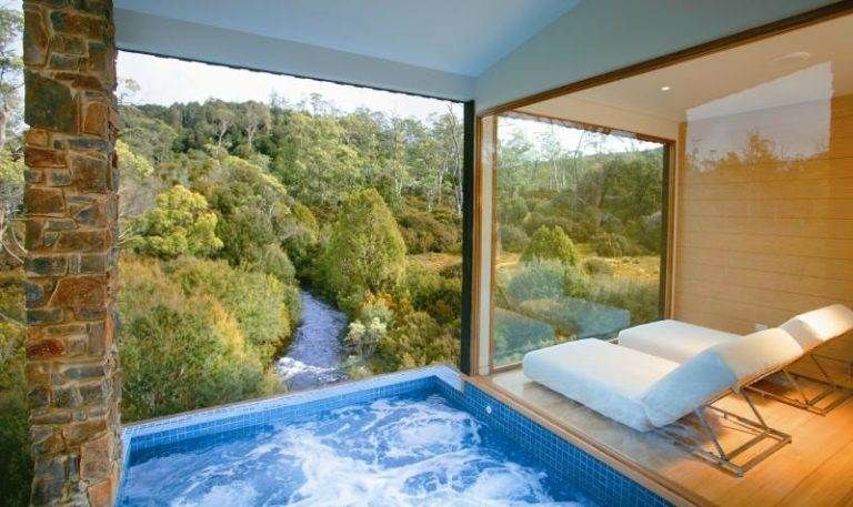 A jacuzzi in a room with a view of a forest at Cradle Mountain Lodge.