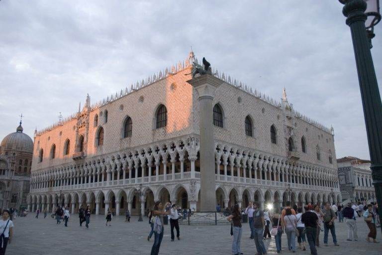 A square with many people walking around in front of an ornate building in Venice.