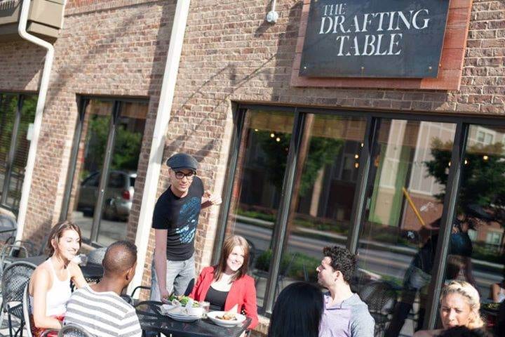 A group of people sitting at The Drafting Table outside of a restaurant.