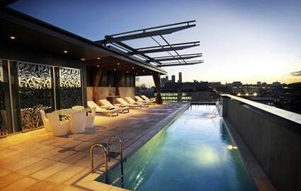A rooftop pool with lounge chairs and a view of the city at Emporium Hotel Brisbane.