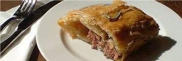 A plate with a piece of meat pie and a fork, offering an exclusive dining experience with sausage rolls.