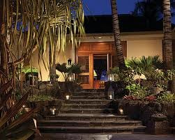 The entrance to a Hawaiian resort at night, surrounded by palm trees.
