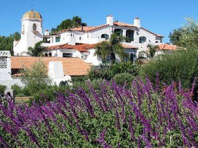 A white house embellished with purple flowers in front.