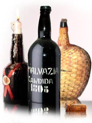 A vintage bottle of Madeira wine and a candle on a table.