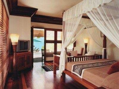 A bedroom with a canopy bed and wooden floors in Kanuhura Resort.