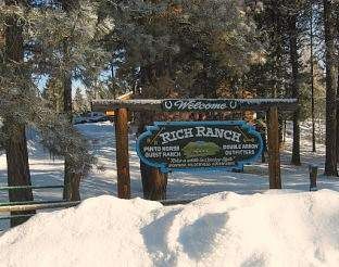 A sign with snow on it in front of a lodge in Montana's Hooked on Snowmobiling::Glacier Country.