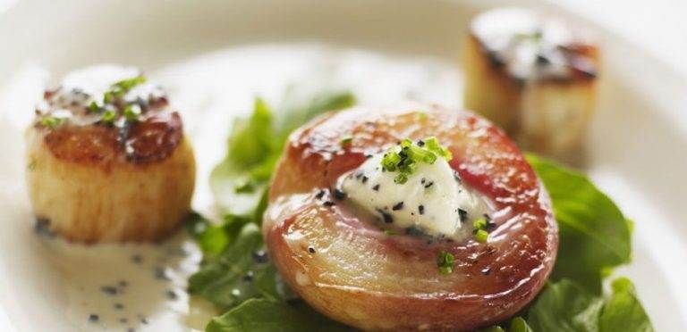 Savor authentic American taste at The Orange Hill Restaurant with a plate of scallops and spinach on a white plate.