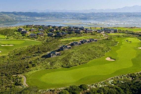 An aerial view of a golf course with mountains in the background at Pezula Resort Hotel & Spa, the ultimate destination for relaxation and luxury.