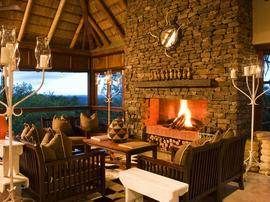 A living room with a fireplace and a view of the savannah, creating intimacy with wildlife from Phinda Mountain Lodge.