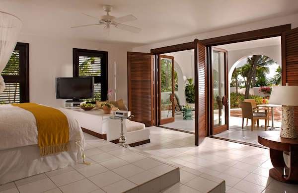 A bedroom with a large bed and a balcony in Cap Juluca, showcasing Moorish architecture surrounded by nature.