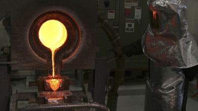 A man in a mask is pouring molten metal into a furnace at the Gold Factory.