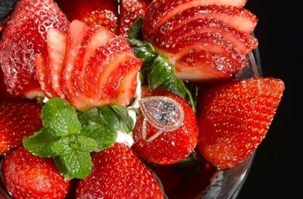 A bowl of strawberries with a diamond ring in it, offering a delicious dessert experience.