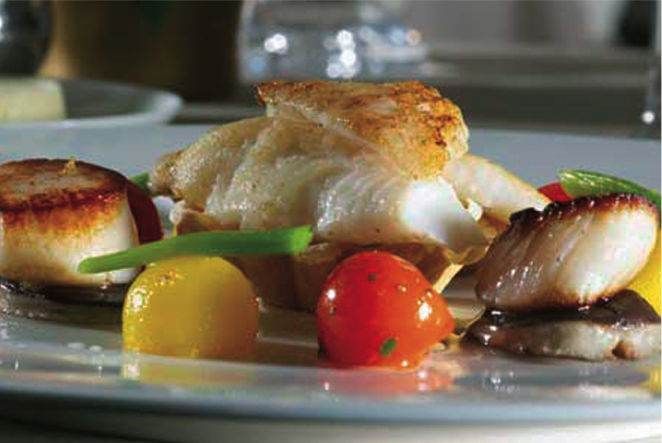 A plate with scallops and tomatoes on it at Pophams Restaurant, known for their authentic British preparations.