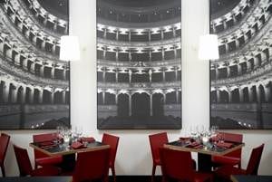 A restaurant with red chairs and a large painting on the wall where you can enjoy the show in the wine theatre.