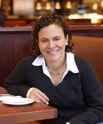 A woman smiling at a table in a restaurant with planned restaurant openings.