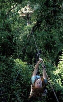 A woman is zip-lining through the jungle.