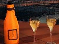 A bottle of Veuve Clicquot champagne and two glasses on a balcony overlooking the city.
