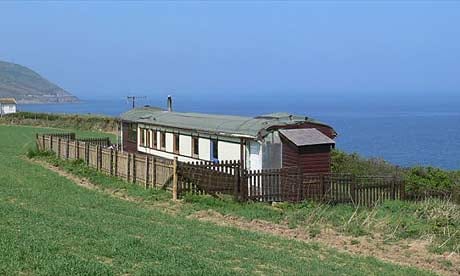 A small caravan on a grassy hill next to the ocean in Wales.