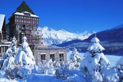 A snow covered building in front of a snow covered mountain, showcasing the grandeur of Badrutt's Palace.