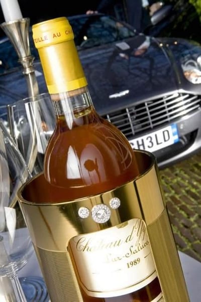 A bottle of Diamond studded La-Fraicheur wine cooler is sitting on a table next to a car.