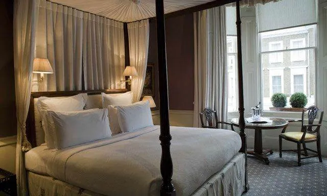 A four poster bed in a room with a window perfect for a Girlfriend Getaway pt.2 in London.