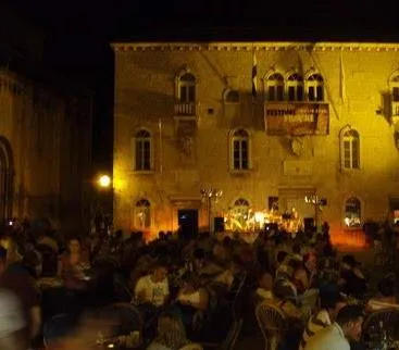 A crowd of people sitting at tables in front of a building at night in Trogir, Croatia.