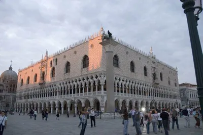 A square with many people walking around in front of an ornate building in Venice.