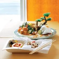 A plate of sushi with chopsticks on a table in front of a window.