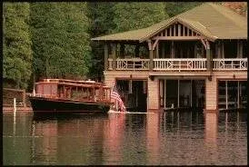 A boat is docked in front of a house on a lake, offering luxe camping at Rockerfeller's lodge.
