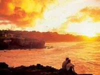 Two people embracing nature, sitting on a rock overlooking the ocean at sunset at the Villas of Kapalua Resort.