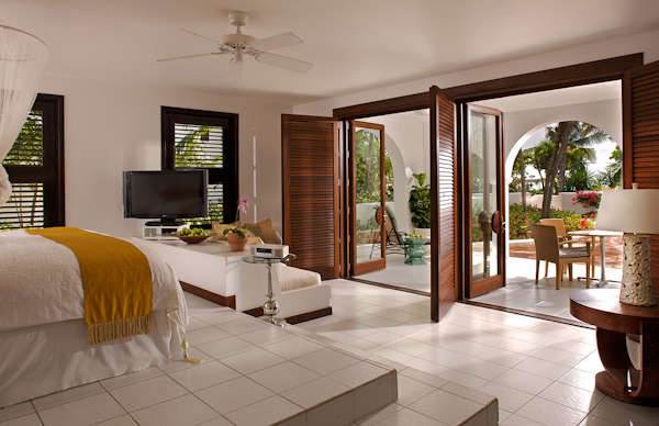 A bedroom with a large bed and a balcony in Cap Juluca, showcasing Moorish architecture surrounded by nature.